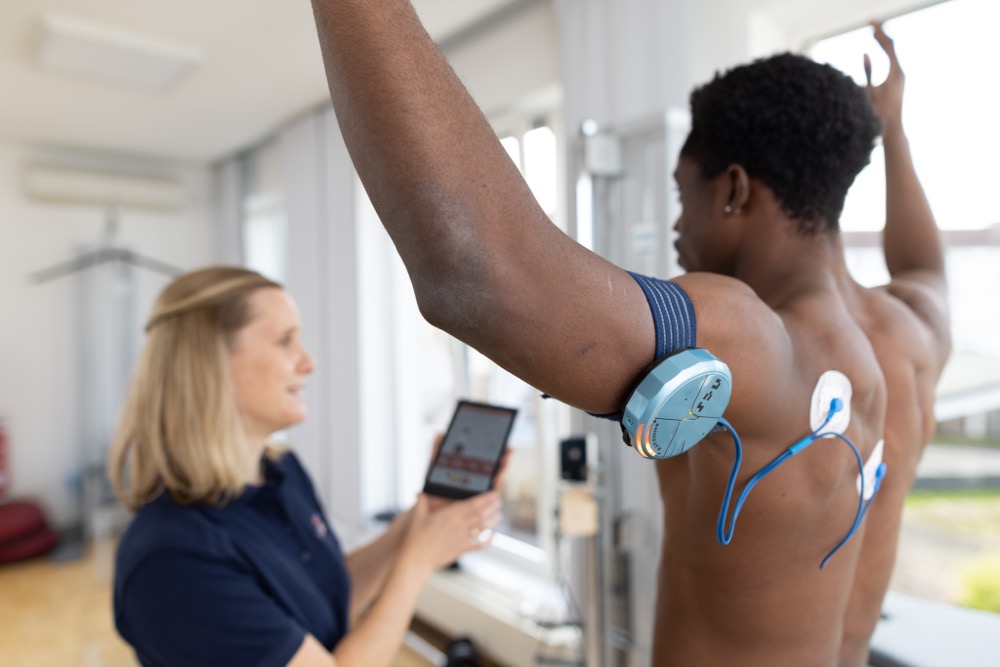 Ein Mann lässt sich in der Physiotherapie in Münster von einer Mitarbeiterin Übungen mit einem Terraband zeigen.