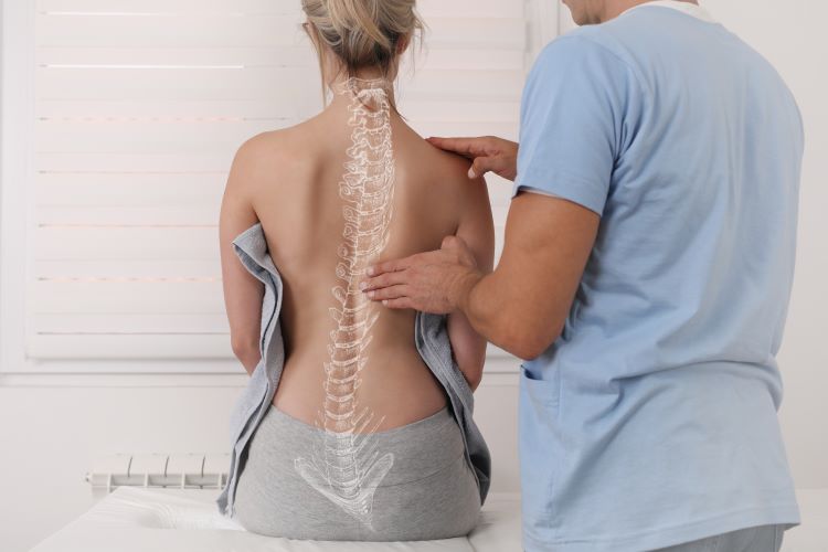 Eine Frau sitzt mit dem Rücken zum Arzt. Der Arzt behandelt ihre Wirbelsäule, welche als Abbildung auf ihrem Rücken zu erkennen ist. 